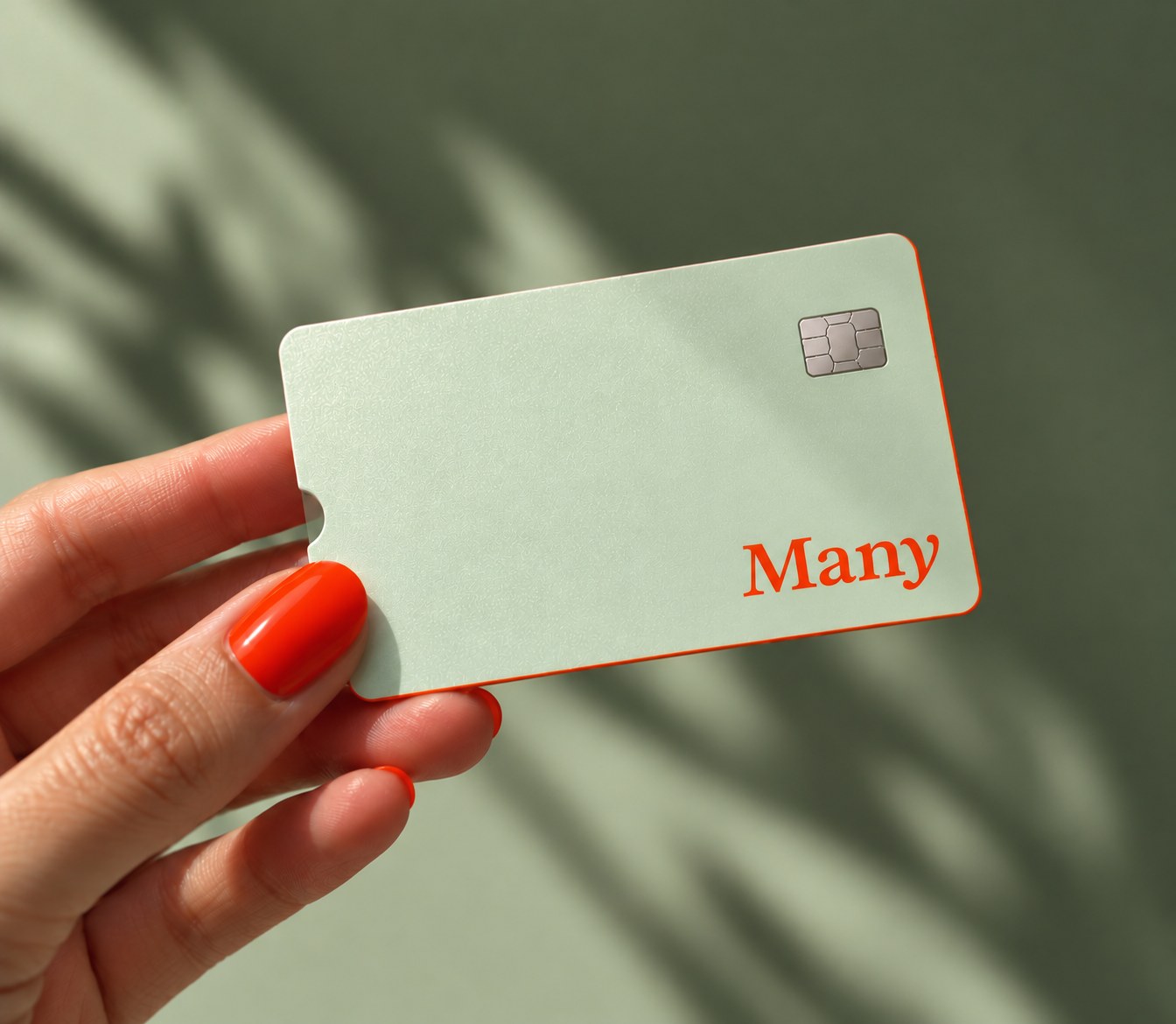A hand with orange nails holding the Many card against a sage wall with leaf shadows